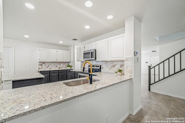 kitchen featuring kitchen peninsula, sink, light stone counters, appliances with stainless steel finishes, and white cabinets