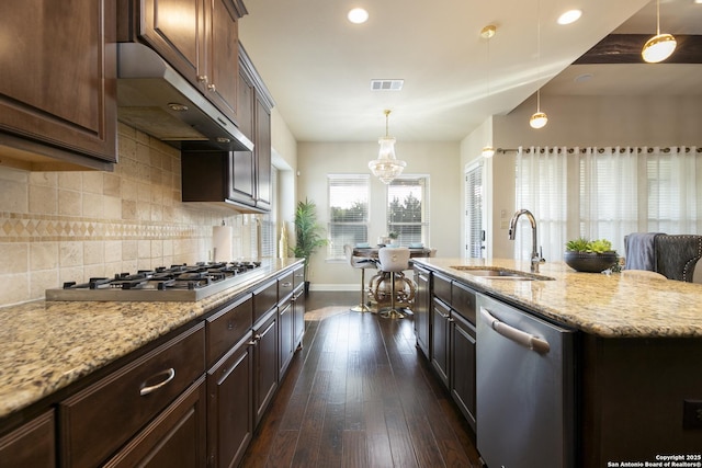 kitchen with stainless steel appliances, decorative light fixtures, light stone countertops, sink, and dark wood-type flooring