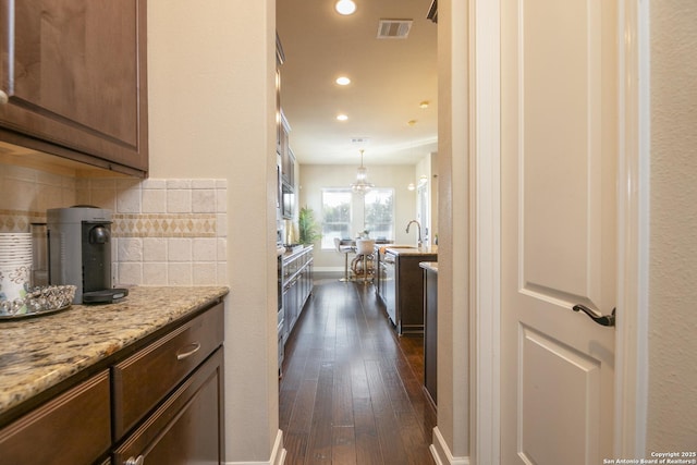 kitchen featuring pendant lighting, dark hardwood / wood-style floors, dark brown cabinets, light stone countertops, and tasteful backsplash