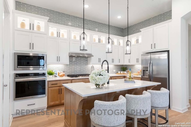 kitchen featuring appliances with stainless steel finishes, white cabinetry, hanging light fixtures, a kitchen island with sink, and decorative backsplash