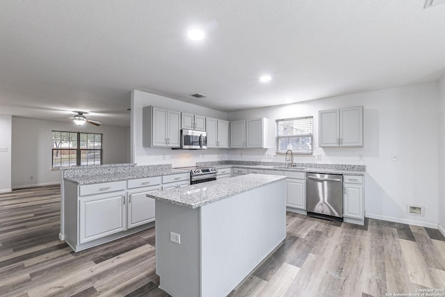 kitchen with appliances with stainless steel finishes, gray cabinetry, a kitchen island, sink, and kitchen peninsula