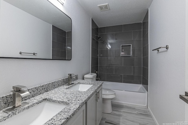 full bathroom featuring a textured ceiling, toilet, vanity, and tiled shower / bath