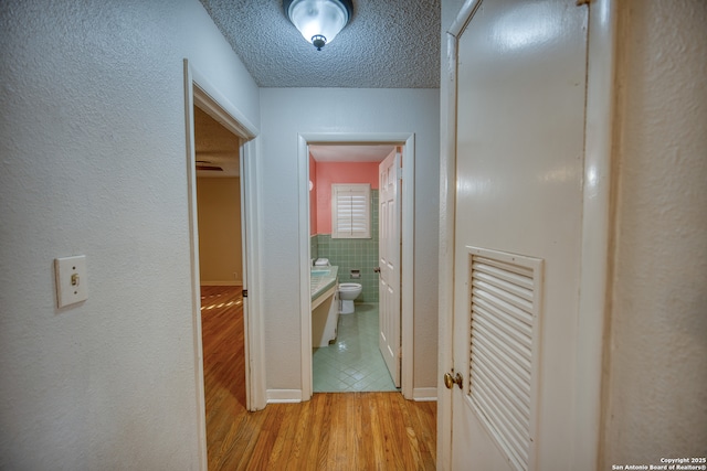 hallway with light hardwood / wood-style flooring, tile walls, and a textured ceiling