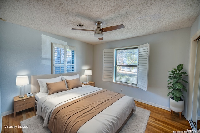 bedroom with hardwood / wood-style flooring, ceiling fan, multiple windows, and a textured ceiling