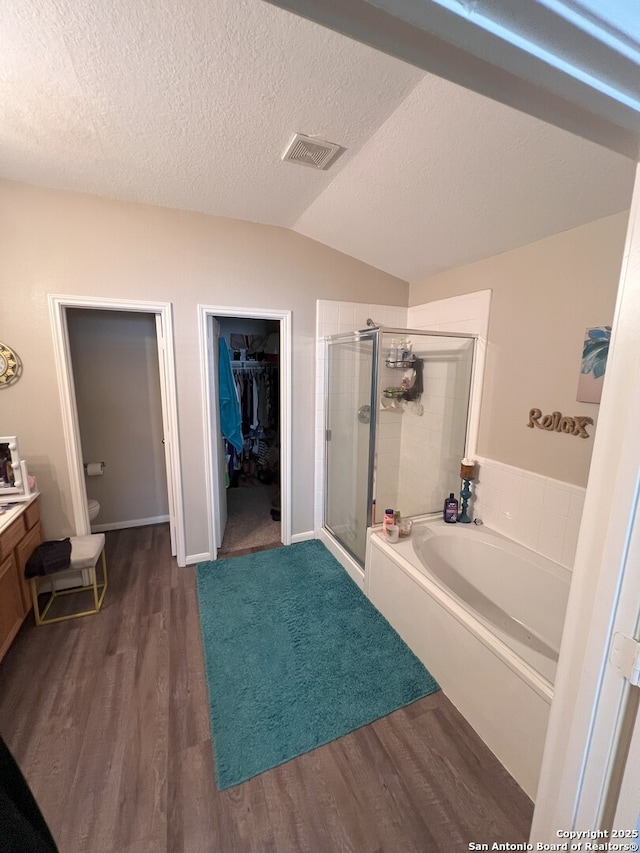 full bathroom featuring toilet, wood-type flooring, a textured ceiling, lofted ceiling, and independent shower and bath