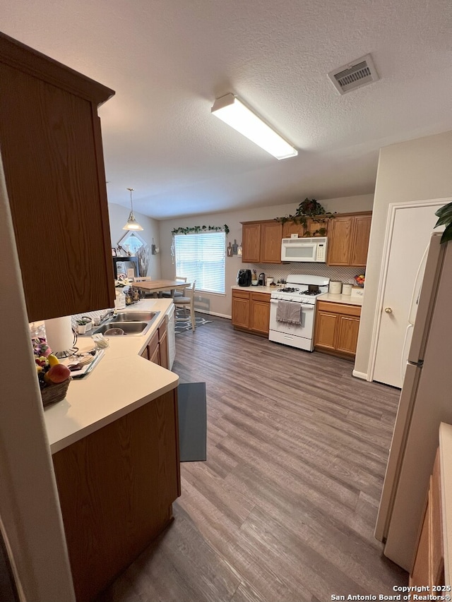 kitchen with kitchen peninsula, white appliances, hanging light fixtures, and dark wood-type flooring