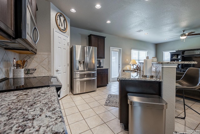 kitchen featuring stainless steel appliances, dark brown cabinetry, sink, light stone counters, and a kitchen bar