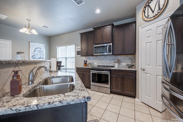 kitchen with decorative light fixtures, light stone countertops, sink, backsplash, and appliances with stainless steel finishes