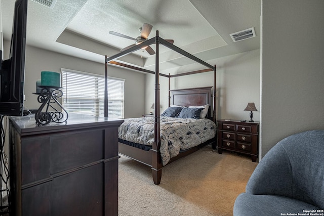 bedroom with ceiling fan, a textured ceiling, a tray ceiling, and light colored carpet