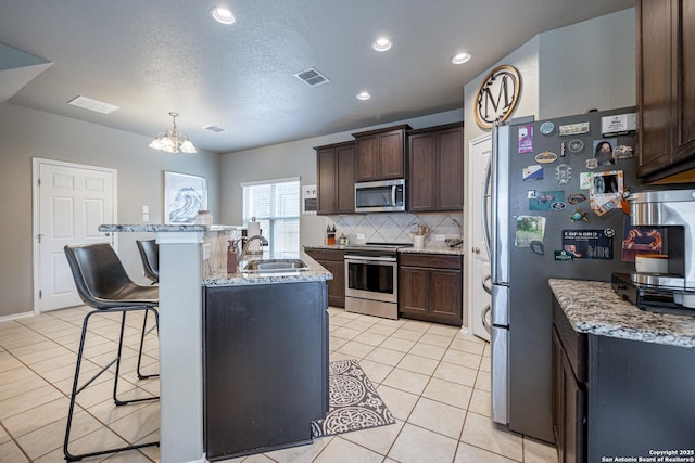 kitchen featuring light tile patterned floors, sink, light stone counters, stainless steel appliances, and dark brown cabinets