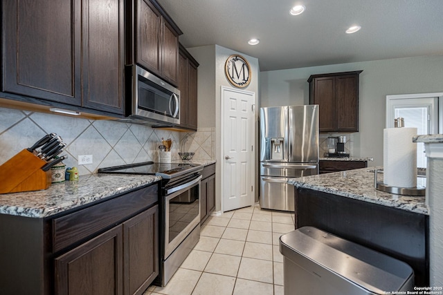 kitchen with appliances with stainless steel finishes, tasteful backsplash, dark brown cabinets, light stone counters, and light tile patterned floors