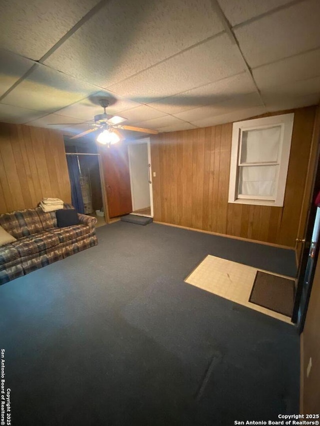 unfurnished living room featuring ceiling fan, wood walls, carpet, and a paneled ceiling