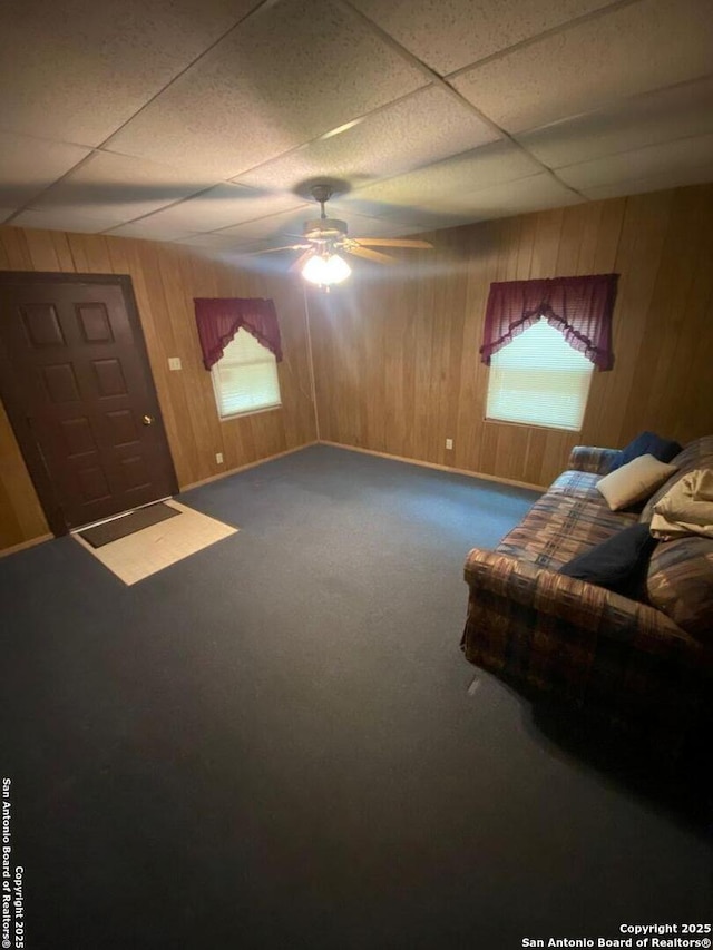 carpeted living room featuring a paneled ceiling, wood walls, and a ceiling fan