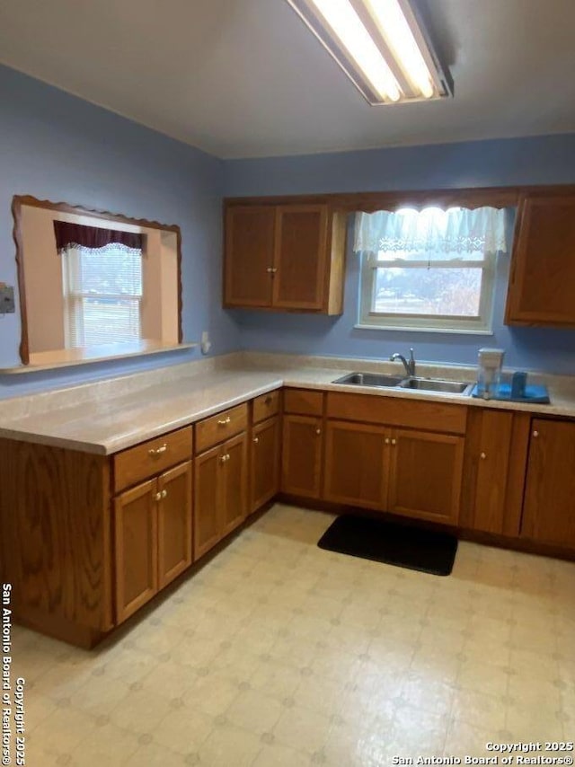 kitchen with brown cabinetry, light countertops, a sink, and light floors