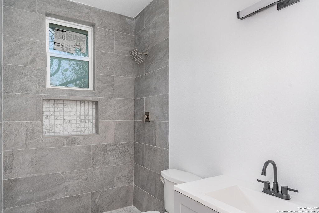 bathroom featuring vanity, a tile shower, and toilet