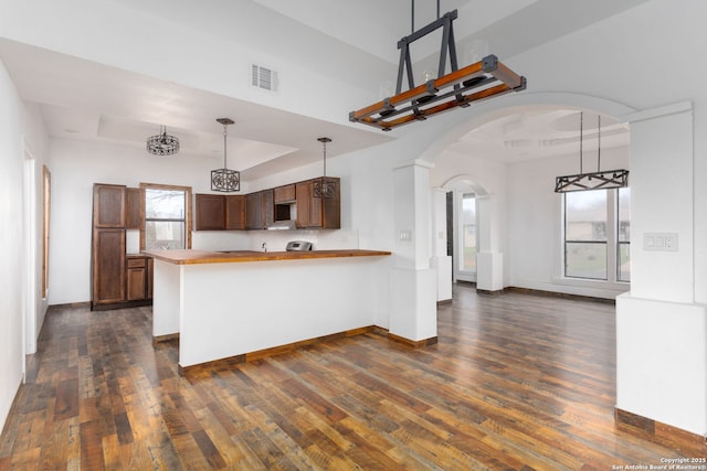 kitchen with pendant lighting, a healthy amount of sunlight, dark hardwood / wood-style flooring, kitchen peninsula, and a raised ceiling