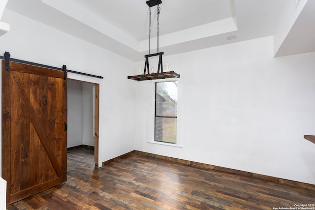 unfurnished dining area with a tray ceiling, a barn door, and dark hardwood / wood-style floors