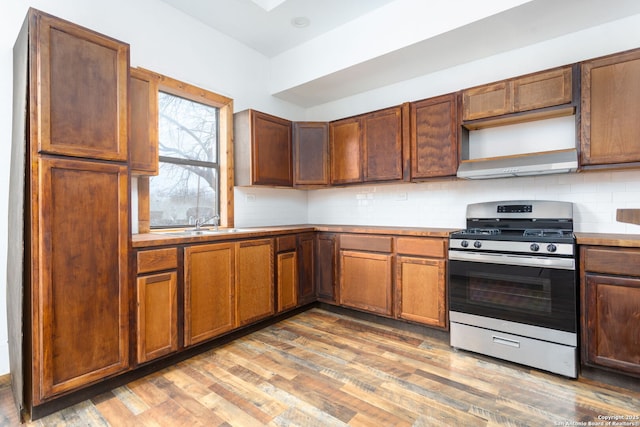 kitchen with gas stove, sink, tasteful backsplash, hardwood / wood-style floors, and wall chimney exhaust hood