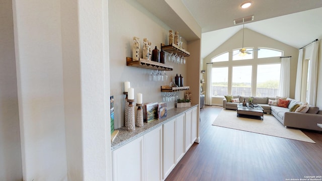 bar featuring dark wood-type flooring, vaulted ceiling, white cabinets, and light stone countertops