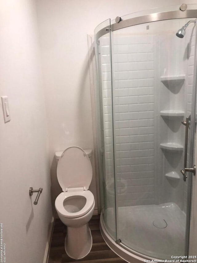 bathroom featuring hardwood / wood-style flooring, a shower with door, and toilet