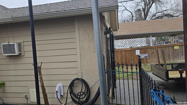 view of home's exterior featuring a shingled roof, fence, and a wall mounted air conditioner