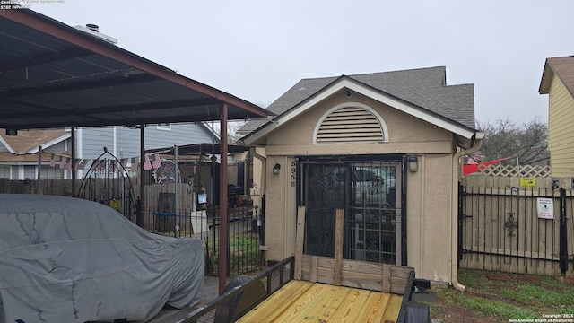 exterior space featuring a shingled roof, fence, an outbuilding, and stucco siding