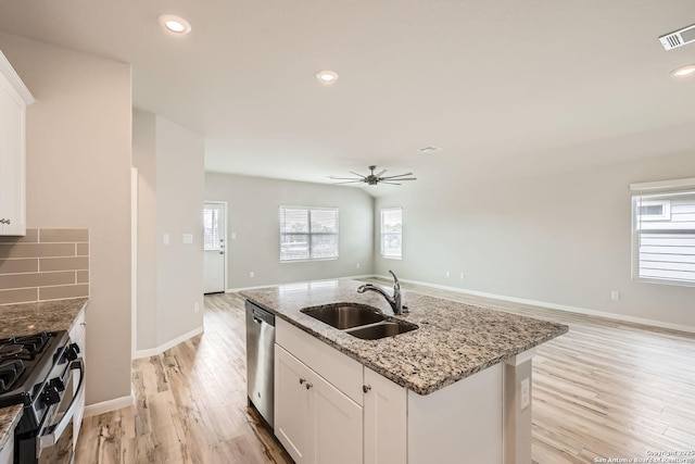 kitchen featuring a center island with sink, gas range, light stone countertops, white cabinetry, and a sink