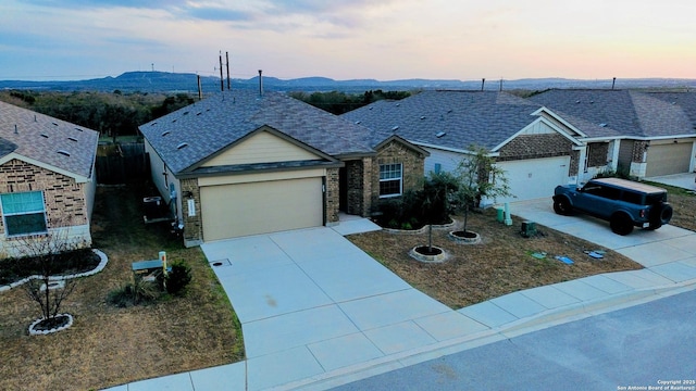 ranch-style house with a mountain view, a garage, a shingled roof, concrete driveway, and stone siding