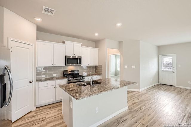 kitchen featuring stainless steel appliances, a sink, visible vents, white cabinetry, and an island with sink