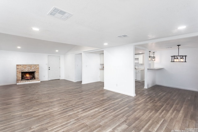 unfurnished living room with lofted ceiling, a brick fireplace, and wood-type flooring