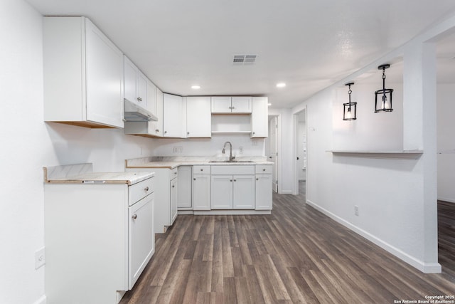 kitchen featuring white cabinetry, kitchen peninsula, hanging light fixtures, sink, and dark hardwood / wood-style floors