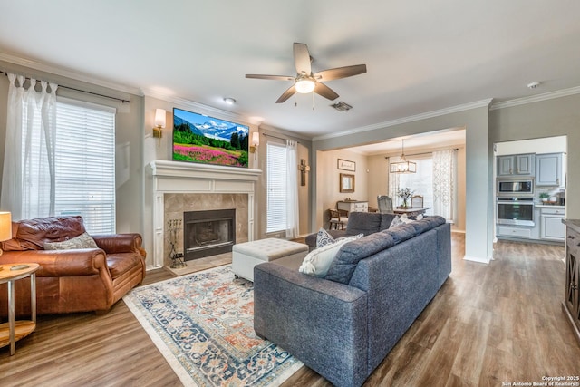 living room featuring a tile fireplace, light wood-type flooring, ceiling fan, and ornamental molding