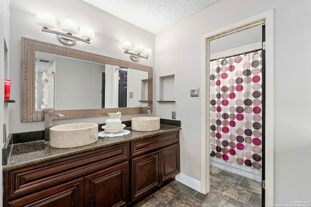 full bath featuring a sink, a textured ceiling, double vanity, and stone finish floor