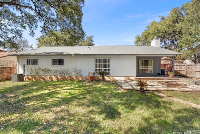 rear view of property featuring central AC unit, a chimney, a yard, and fence