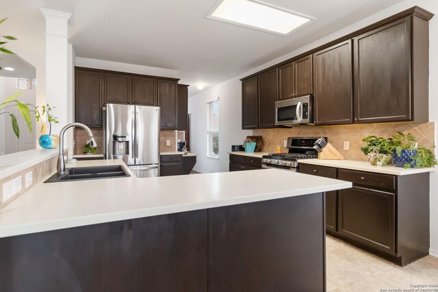 kitchen featuring appliances with stainless steel finishes, sink, kitchen peninsula, dark brown cabinetry, and tasteful backsplash