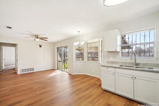 kitchen featuring sink, light stone counters, white cabinetry, light hardwood / wood-style floors, and hanging light fixtures