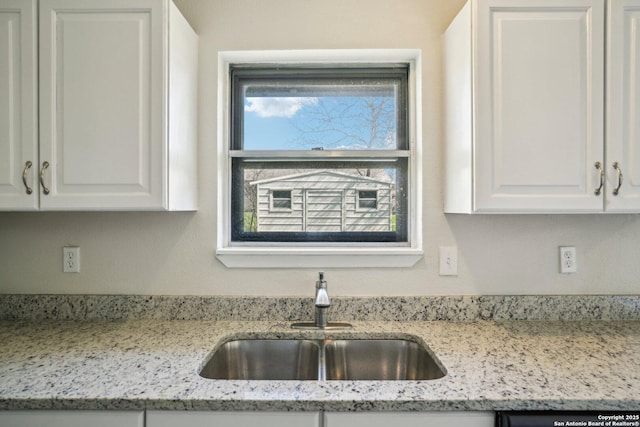 kitchen featuring sink, white cabinets, light stone counters, and dishwashing machine