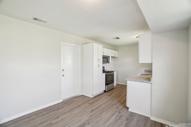 kitchen with white cabinetry, stainless steel appliances, light hardwood / wood-style flooring, sink, and a textured ceiling