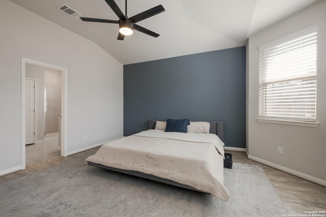 bedroom featuring light hardwood / wood-style floors, vaulted ceiling, ensuite bathroom, and ceiling fan