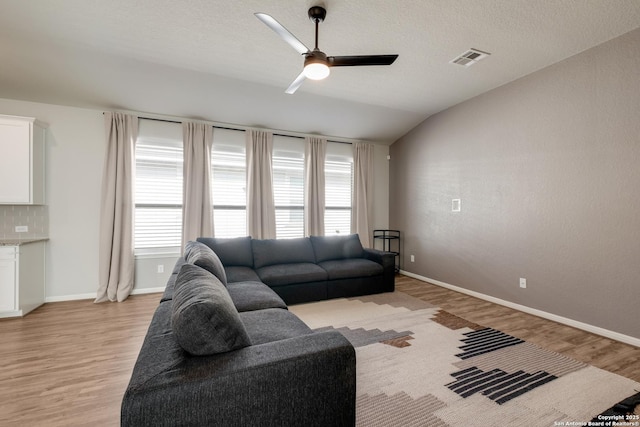 living room with ceiling fan, light hardwood / wood-style flooring, a textured ceiling, and lofted ceiling