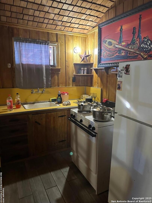 kitchen featuring white gas stove, refrigerator, wood walls, and sink