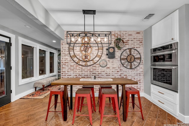 dining area with an inviting chandelier, hardwood / wood-style flooring, and brick wall