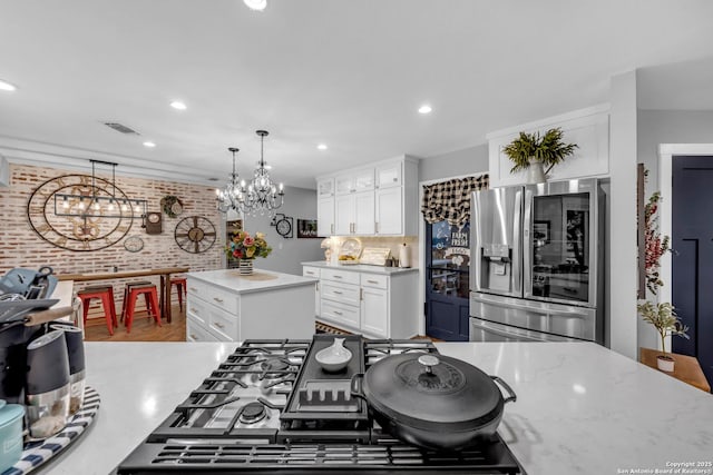 kitchen with hanging light fixtures, brick wall, stainless steel refrigerator with ice dispenser, a kitchen island, and white cabinetry