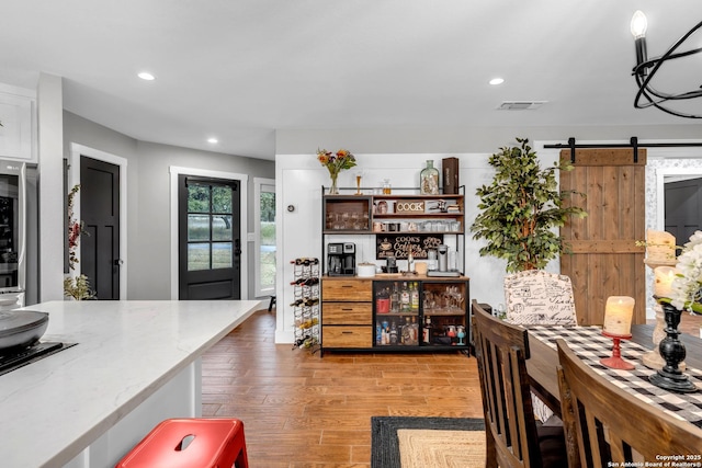 kitchen featuring wood-type flooring, beverage cooler, a barn door, and light stone counters