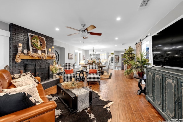 living room featuring a fireplace, hardwood / wood-style floors, ceiling fan, and a barn door