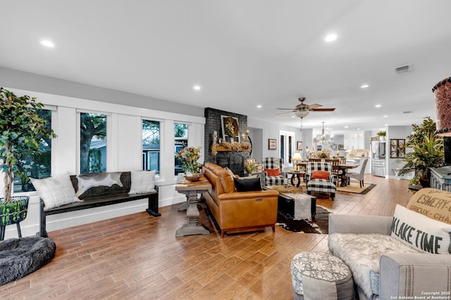 living room with ceiling fan with notable chandelier, light wood-type flooring, and a fireplace