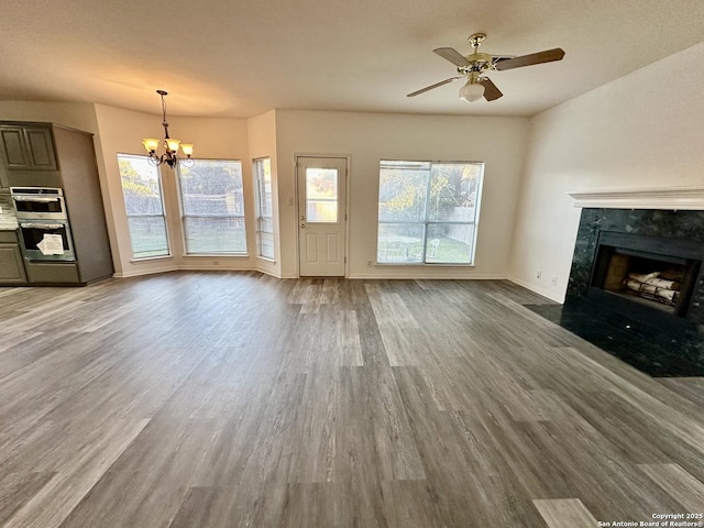 unfurnished living room featuring ceiling fan with notable chandelier, a high end fireplace, a wealth of natural light, and wood-type flooring