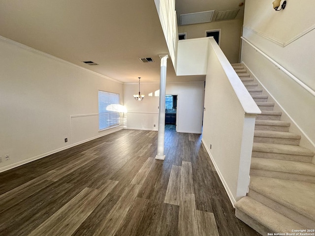 unfurnished living room featuring crown molding, an inviting chandelier, and dark wood-type flooring