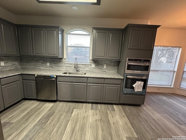 kitchen with light wood-type flooring, sink, gray cabinets, tasteful backsplash, and dishwasher