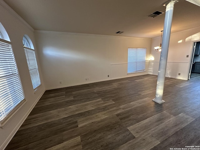 empty room featuring decorative columns, ornamental molding, a chandelier, and dark hardwood / wood-style floors